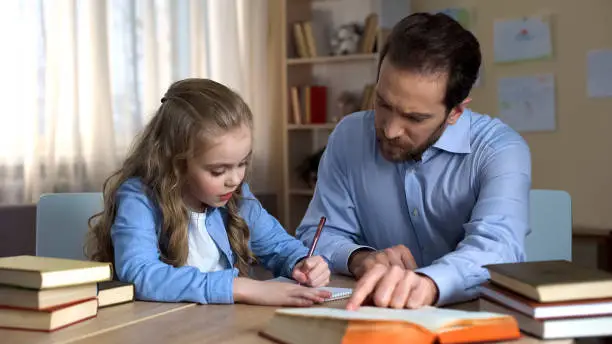 Attentive father helps his little daughter to do homework, education process