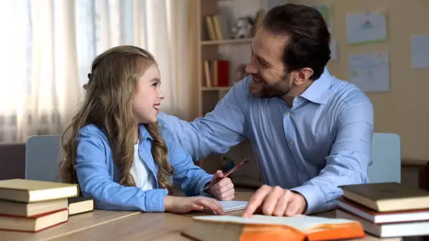 Happy female child doing homework with her caring daddy, support and love