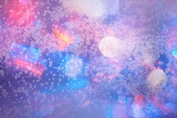 Winter background in soft pastel colors. Frost and snowflakes on the window. Multicolored bokeh with blur.