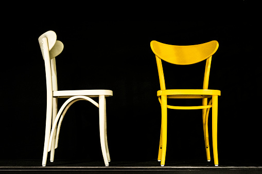 Two old-fashioned wooden chairs of different colors (white and yellow) on a black background