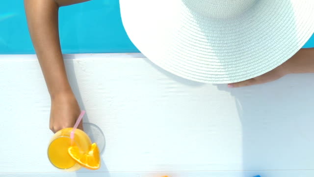 Woman in big hat swimming and drinking cocktail at pool bar, luxury resort spa