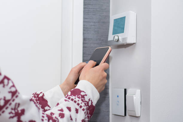 Girl adjusts and regulate the room temperature with smart phone on switch wall Young woman adjusts and regulate the room temperature with smart phone on switch wall. Smart WiFi light switch and temperature regulator. Smart house concept. Close up, selective focus telephone access control system stock pictures, royalty-free photos & images