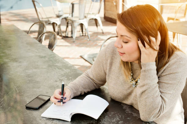 Latina Female Millennial Journals Her 2019 New Years Resolutions A young woman writes her 2019 New Years Resolutions in a journal 2019 new year resolution stock pictures, royalty-free photos & images