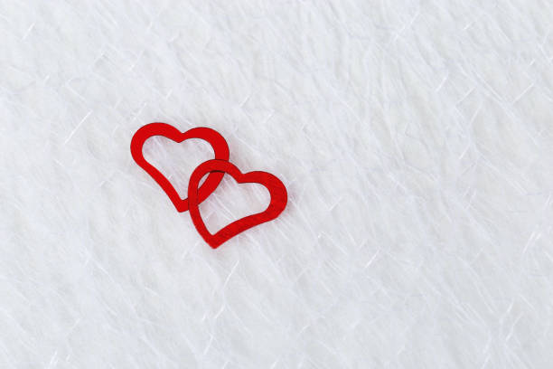 Two bright red hearts on a white blurred translucent fabric. Greeting card, background or invitation with copy space for text. Flat lay.