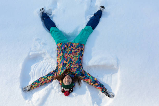 высокий угол зрения счастливой девушки, лежащей на снегу и двигая руками и ногами вверх и вниз, создавая фигуру снежного ангела. улыбающаяс� - 13425 стоковые фото и изображения