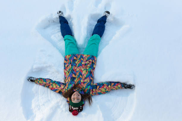 vista ad alto angolo di ragazza felice sdraiata sulla neve e che muove braccia e gambe su e giù creando una figura di angelo della neve. donna sorridente sdraiata sulla neve in vacanza invernale con spazio di copia - 13431 foto e immagini stock