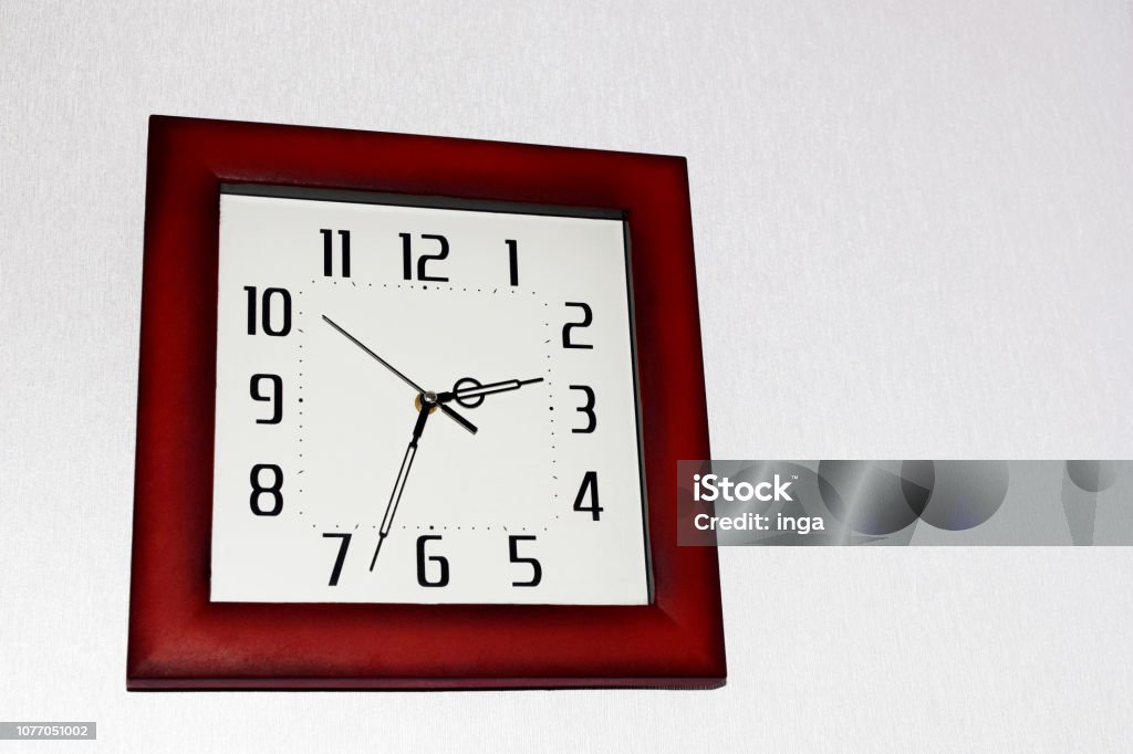Square shape wall clock Square shape wall clock with white dial and red brown frame on very light grey background with copy space for text. Alarm Stock Photo