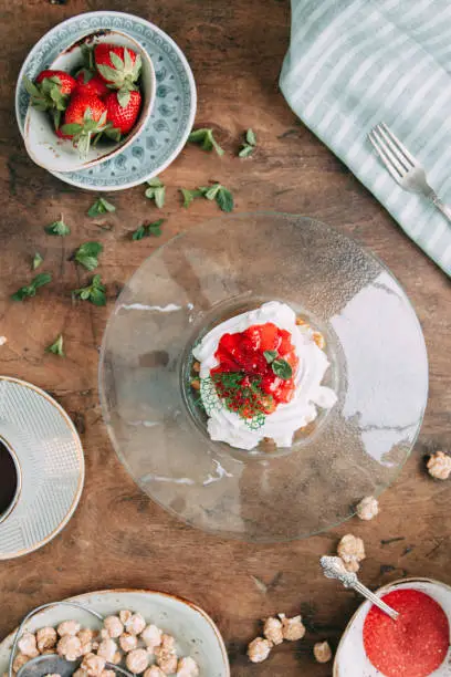 Pavlova dessert with berries in a beautiful composition. Foodstyling on a wooden background with coffee and strawberries.