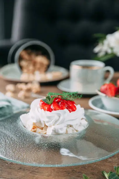Pavlova dessert with berries in a beautiful composition. Foodstyling on a wooden background with coffee and strawberries.