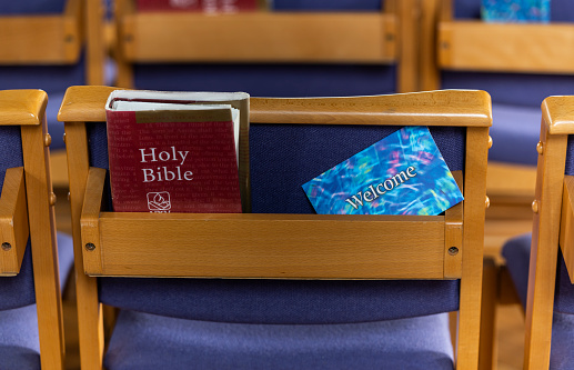 Brockenhurst, England - October 23, 2018: Red holy bible and welcome invitation on a blue chair in the church of Brockenhurst.