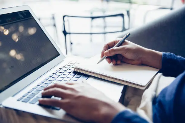 Photo of Business man working on laptop computer and writing notebook.