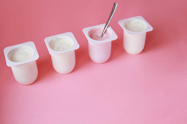 istock Four yogurts in white plastic cups on pink background with copy space.Minimal style. 1077073380