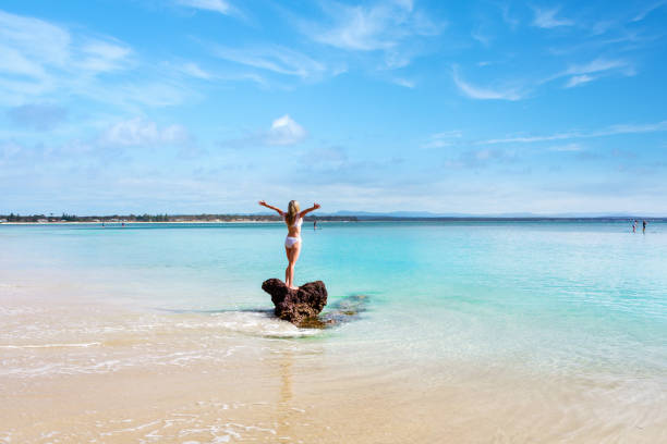 Female on holiday in white swimsuit cozzie, standing on a rock surrounded by the beautiful pristine waters of Jervis Bay Australia.  Space for copy