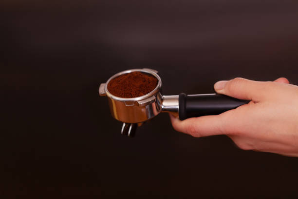 Man is using a tamper to press freshly ground morning coffee into a coffee tablet