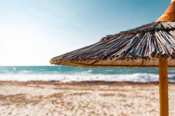 Close up shot with shallow depth of field of a straw made tropical beach umbrella in front of a defocussed turquoise sea.