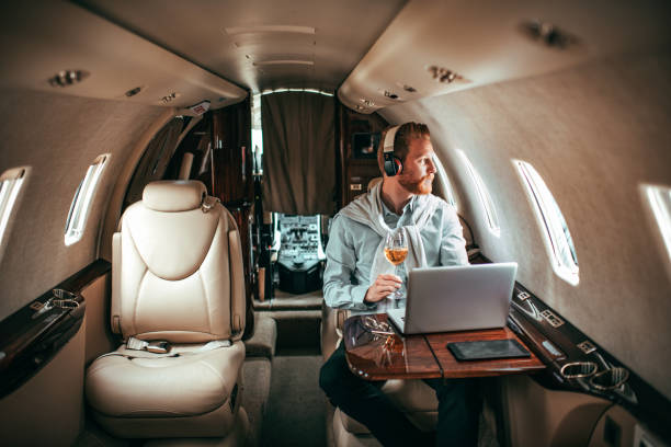 riche jeune homme appréciant un verre de vin et d’écouter de la musique via le casque tout en étant assis dans un jet privé - status symbol audio photos et images de collection