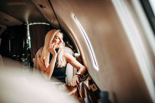 Beautiful young businesswoman talking on a mobile phone while traveling in a private airplane Beautiful blonde businesswoman having a phone conversation while sitting in a private jet. She is looking through the window. exclusive travel stock pictures, royalty-free photos & images