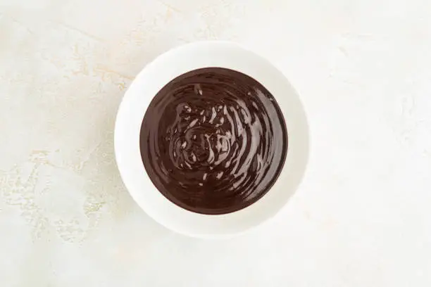 Melted chocolate, cream, ganache in white ceramic bowl, top view