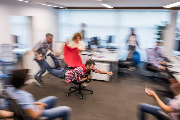 Group of playful colleagues having fun in blurred motion at casual office. Young man pretending to be a superhero while having fun with his colleagues on a break in the office. Blurred motion. push pause stock pictures, royalty-free photos & images
