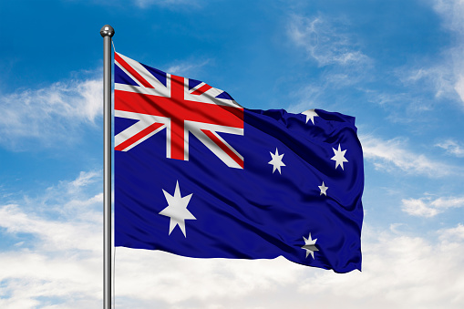 Flag of Australia waving in the wind against white cloudy blue sky. Australian flag.