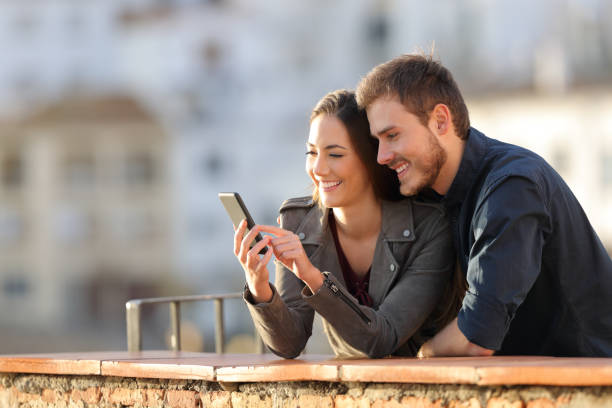istock Happy couple using phone in a balcony at sunset 1077099780