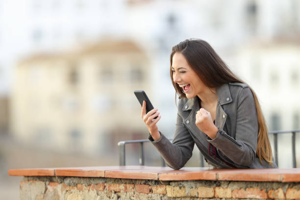 istock Excited woman checking smart phone in a balcony 1077100036