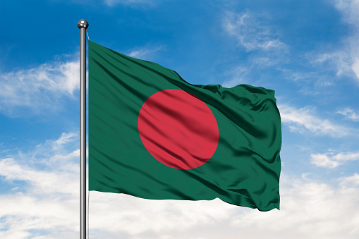 Flag of Bangladesh waving in the wind against white cloudy blue sky. Bangladeshi flag.