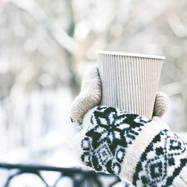 istock Female hands in white and black mittens holding steaming  cup 1077100748