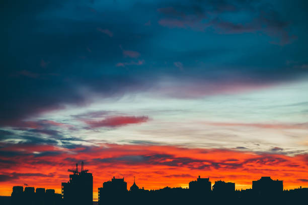 istock Cityscape with wonderful varicolored vivid dawn. Amazing dramatic multicolored cloudy sky above dark silhouettes of city buildings. Atmospheric background of sunrise in overcast weather. Copy space. 1077109246