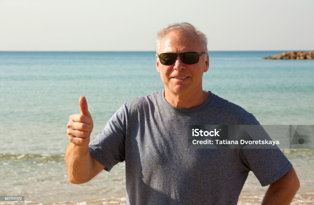 A man over 60 years shows a gesture all right Portrait of a man over 60 years old. Elder man shows gesture - all right. Hi was shot close-up against the sea on a Sunny day. The man is wearing sunglasses and a t-shirt. Hi in good physical shape, he smiles. Men Stock Photo