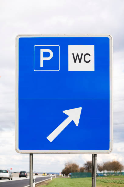 a hexagonal parking sign with a white background, blue border, large blue 'P' on the right, and a black left-pointing arrow on the left, attached to a brick wall.
