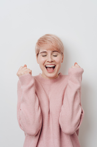 Excited exultant young blond woman cheering clenching her fists and yelling over a white studio background