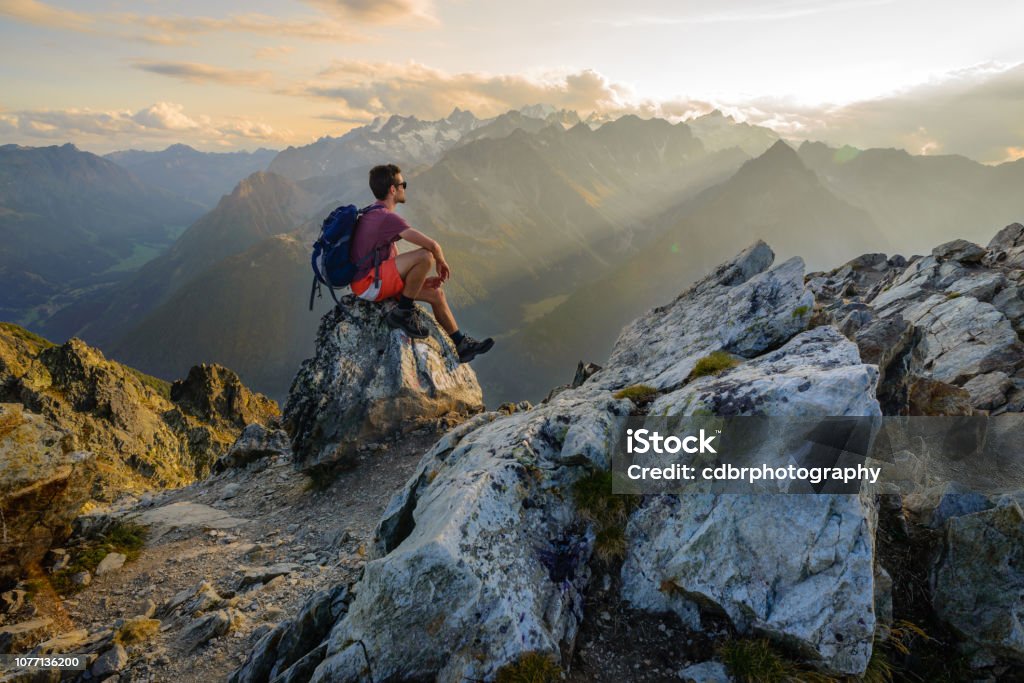 Sunset hiking scenery in the mountains A man sitting on a rock at the summit of a mountain, admiring the scenery after a long hike. Hiking Stock Photo
