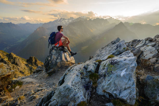 Sunset hiking scenery in the mountains A man sitting on a rock at the summit of a mountain, admiring the scenery after a long hike. chamonix photos stock pictures, royalty-free photos & images