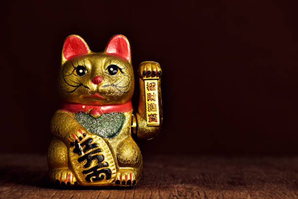 chinese lucky cat a golden chinese lucky cat with its left paw raised, on a rustic wooden surface maneki neko stock pictures, royalty-free photos & images