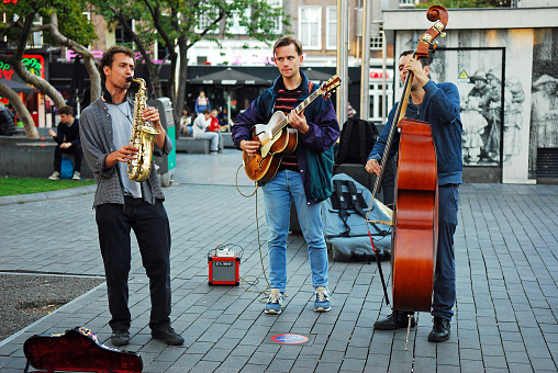 Three young street musicians playing jazz music on Rembrandt Square in the center of Amsterdam