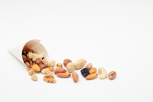 Assorted  Nuts  spill out of a paper cone on white background close up High angle view