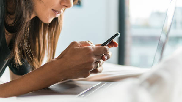 istock Young woman texting while using laptop by hotel room window 1077165744