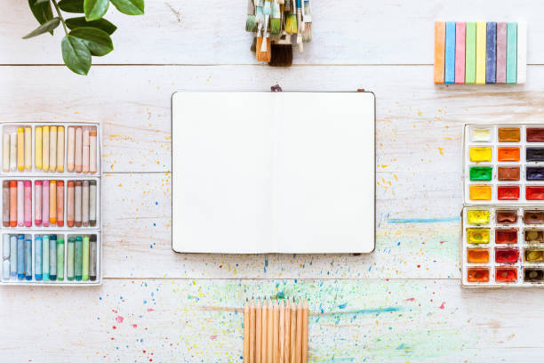 istock Paint brushes set, paintbox with watercolors, crayons, pencils and open notebook paper on white wooden background, artistic creative art workplace accessories. Top view, flat lay with copy space 1077172358