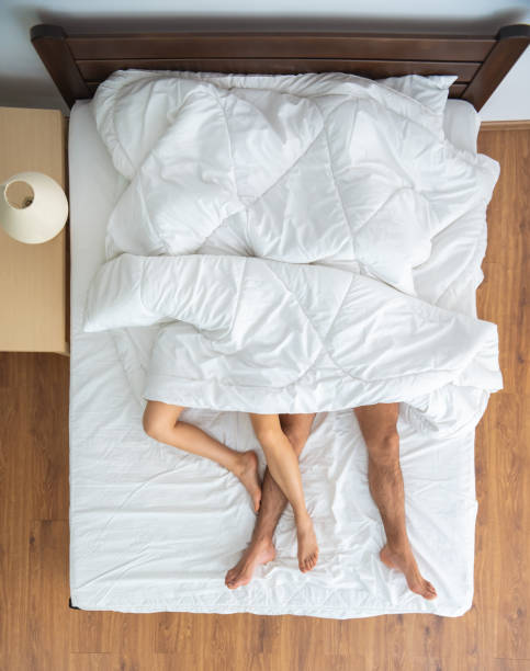 毛布の下のカップルがベッドに横たわっていた。上から見る - bed couple human foot heterosexual couple ストックフォトと画像