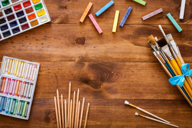 istock Creative art work accessories tools supplies set on messy desk, paint brushes, paintbox watercolors crayons pencils on brown wooden artistic background, back to school. Top view, flat lay, copy space 1077173732
