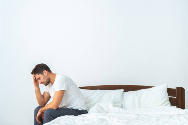 istock The unhappy man sitting on the bed on the white background 1077177296