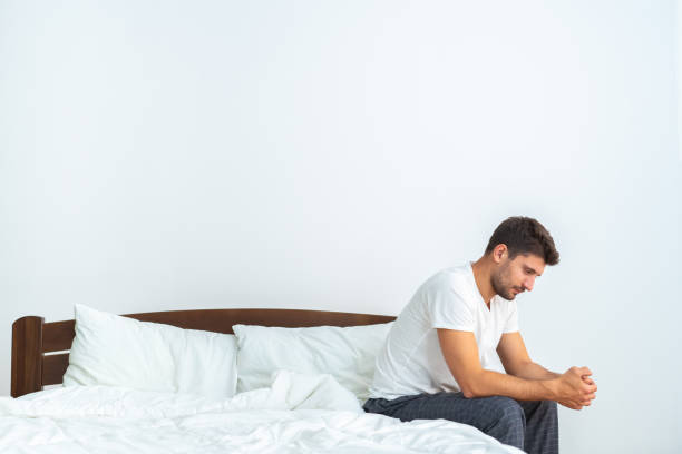 The depressed man sitting on the bed on the white background stock photo
