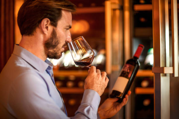 Man tasting and degustating wine in front of a wine cooler