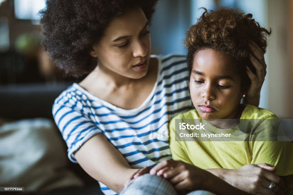 African American mor tröstar henne ledsen flicka hemma. - Royaltyfri Barn Bildbanksbilder