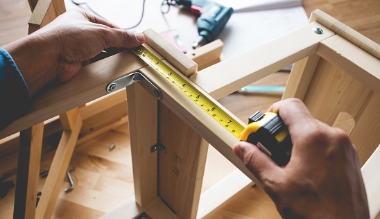 Man assembly wooden furniture,fixing or repairing house with yellow tape measures.