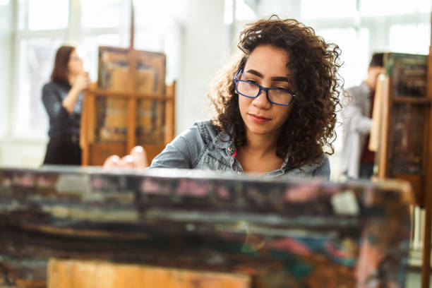 Female high school student making her painting on a class at art studio.