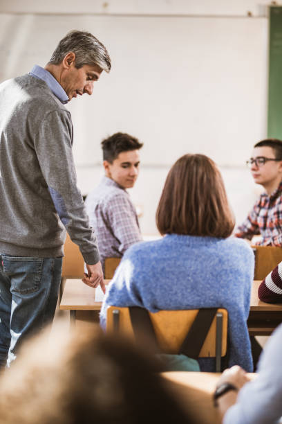 istock Mid adult teacher assisting his students on a class at high school. 1077183030