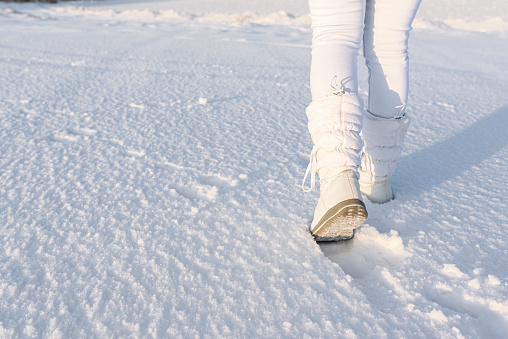 Low angle view of walking away female with white snow boots on, in deep snow. Winter background.