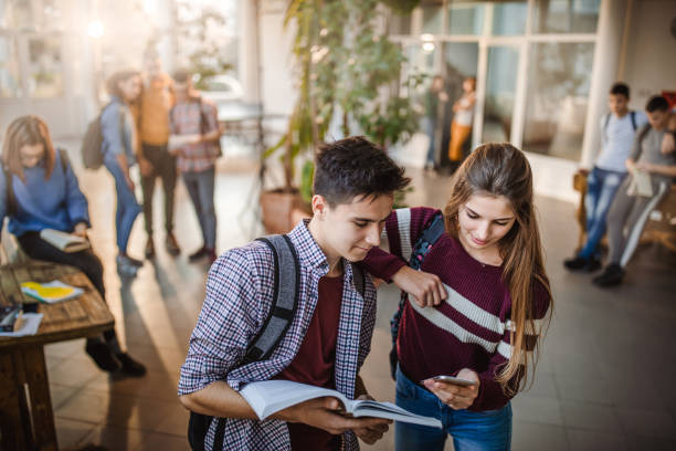 istock Smiling high school couple using cell phone in a hallway. 1077187060